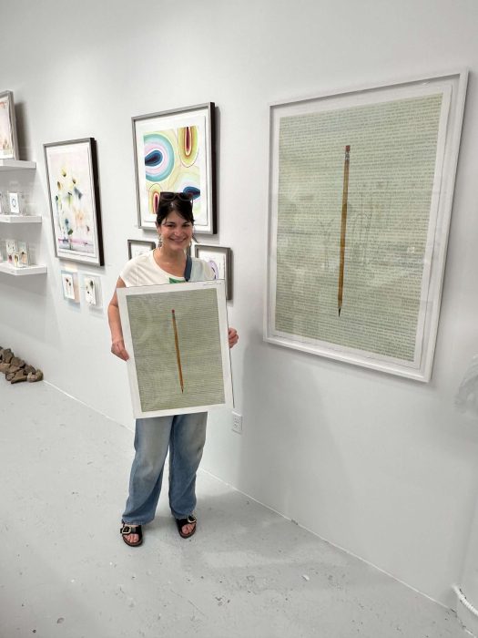 Thoughtful woman at art gallery holding framed artwork titled "Life Demands on Both Ends".